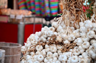 Sarımsak demetlerinin ve geleneksel ahşap varillerin gündüz fotoğrafı arka planda renkli Tayvan ka-ch çantalarıyla klasik bir marketin önünde sergileniyor..
