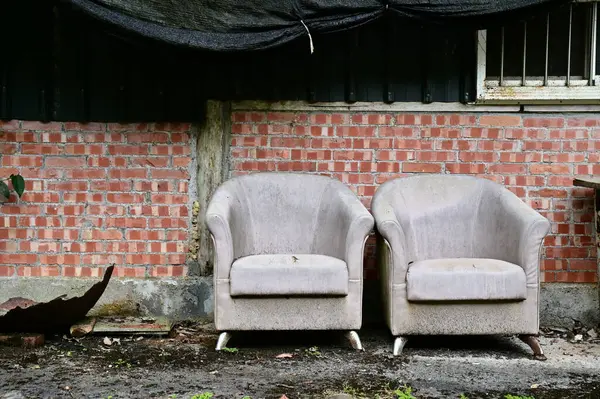 stock image Capture the charm of a weathered red brick house with old sofas outside, evoking nostalgia and tranquility on a cloudy afternoon.