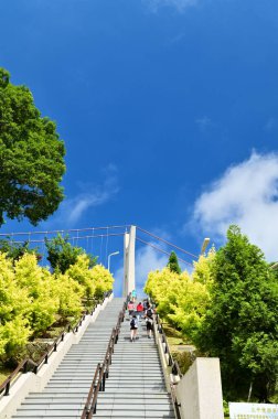 Taiwan - Jul 07, 2024: Enjoy a clear summer day with blue skies and white clouds as people walk towards the entrance of Taiping Cloud Ladder, surrounded by lush greenery. clipart