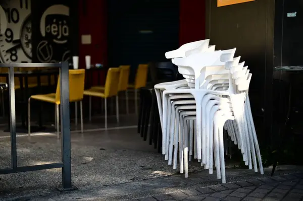 stock image In the morning, sunlight casts a diagonal glow on a stack of white plastic chairs in an outdoor dining area of a restaurant that hasn't opened yet.