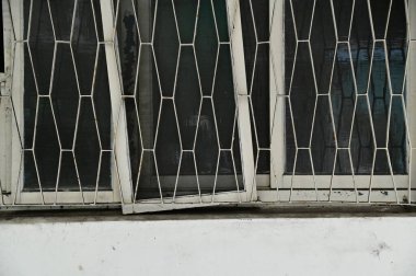 A traditional residential window wwhite-painted wooden frames and iron gratings, found in an urban area marked for redevelopment. A nostalgic glimpse into an architectural style slowly disappearing. clipart