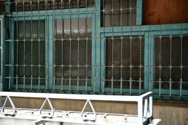 A glass-paneled wooden window with intricate iron grille designs overlooks a corridor adorned with iron flower stands, capturing the nostalgic essence of a soon-to-be-renovated residential complex. clipart