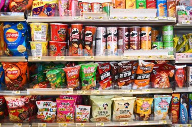 Canlı bir cips, mısır çerezi ve hazır erişte atıştırmalıkları vitrinleri dolduruyor, çeşitli aroma ve dokular sergiliyor..