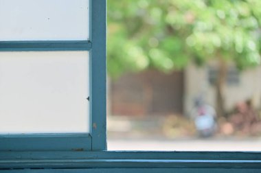 Açık hava yeşili, pencere tasarımı ve kapalı mekan ışıklandırması olan mavi-yeşil sürgülü pencereye yakın plan. Ev dekorasyonu, mimari ve fotoğraf referansları için uygun.