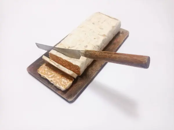 stock image close up of raw tempeh on wooden cutting board and knife cutting tempeh isolated on white background.