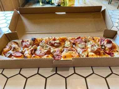 Biftek sosisli, sucuklu, mozzarella peynirli, domates soslu ve mantarlı uzun pizza.