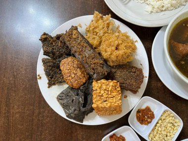 A plate of side dish consists of fried tempeh, cow beef, Potato Perkedel, and Empal in a restaurant clipart