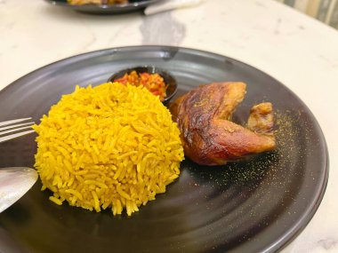 Bir tabak mandi pilavı, acılı sambal ve kızarmış tavuk budu ile servis edilir.