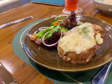 Croque Monsieur ya da kızarmış sandviç, erimiş peynir, jambon ve sebze salatası.