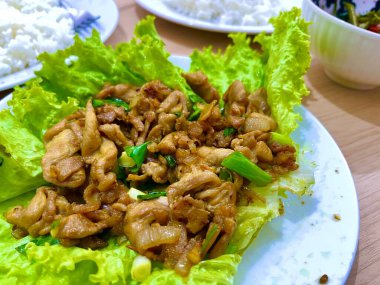 İstiridye soslu tavuk kızartması ve beyaz tabakta marulla servis edilen taze soğan.