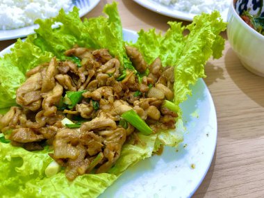 İstiridye soslu tavuk kızartması ve beyaz tabakta marulla servis edilen taze soğan.