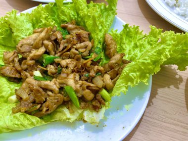 İstiridye soslu tavuk kızartması ve beyaz tabakta marulla servis edilen taze soğan.