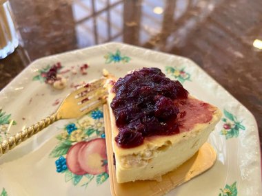 Küçük bir tabakta servis edilen yaban mersini soslu bir dilim peynirli pasta.