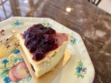 Küçük bir tabakta servis edilen yaban mersini soslu bir dilim peynirli pasta.