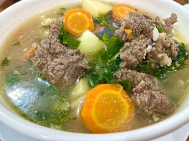 Et pirzolası, havuç, patates ve taze soğanlı çorbanın yakın görüntüsü.