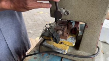 Atölyedeki çilingir orjinalinden anahtar kopyalama makinesi ile yeni anahtarı kopyalıyor.