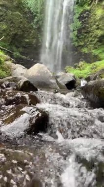 Arka planda şelaleli kaya manzaralı nehir suyunun dikey videosu 