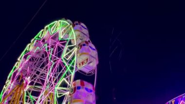 Renkli neon ışığı ve gece gökyüzü olan lunapark dönme dolabı yerel bir karnaval festivalinde dönüyor.