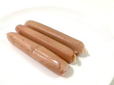 Üç tane pişmemiş, beyaz arka planda plastik kabuklu ucuz tavuk sosisi.