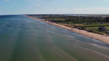 Yazın sahilde güzel bir uçuş. İnsanlar deniz kenarında dinleniyor. Turistler için evler. Plaj şemsiyeleri, gezintiler, denizde yüzen insanlar..