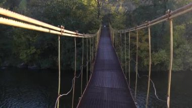 Nehrin üzerinde asılı demir köprü boyunca yürü. Demir asma köprü sallanıyor. Köprünün altından bir nehir akıyor. Nehrin diğer tarafındaki sonbahar ormanı. Aydınlığın ışıkları, akşam