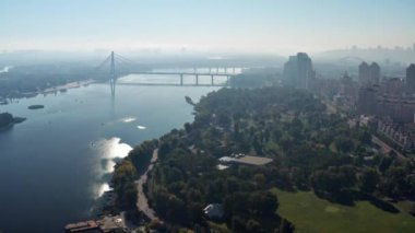 Kyiv ve Dinyeper Nehri üzerinde güzel bir uçuş. Güneş nehire yansıyor. Arka planda nehir boyunca sis ve köprü var. Dinyeper seti boyunca çok katlı binalar..