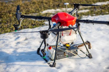 Sahada güzel bir kırmızı agrodron duruyor. Buğday yetişiyor. Kar henüz erimedi ki. Agrodronlar gübre püskürtmeye hazır..