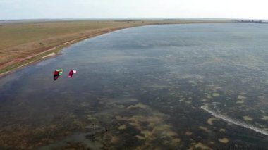 İnsanlar denizde uçurtma gibi uçuyor. Rüzgar sporcuyu deniz dalgaları boyunca taşır. Çok renkli paraşütler.