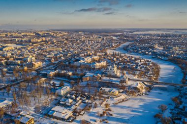 Kış şehrinin güzel manzarası. Karda evler ve binalar. Köprü nehrin üzerinde. Ortodoks kiliseleri ve Katolik katedrali. Nehir buzla kaplı..