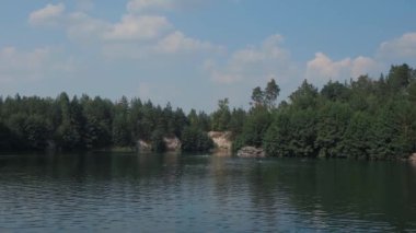 Yazın güzel bir göl. Uzaktaki insanlar gölde yüzüyorlar. Tüm sahil yeşil yapraklı ağaçlarla kaplı. Güzel taş plaj. Bir yaz gününde nehir.