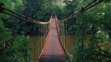 Nehrin üzerinde asılı demir köprü boyunca yürü. Demir asma köprü sallanıyor. Köprünün altından bir nehir akıyor. Nehrin diğer tarafındaki sonbahar ormanı. Aydınlığın ışıkları, akşam