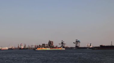 Gemiler Kuzey Denizi boyunca yüzer. Arka planda yel değirmenleri var. Ağır çekim. Hollanda 'daki deniz limanı. Malzeme yüklemek için bir sürü vinç. Farklı gemiler ve mavnalar..