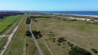 Sahildeki kijkduin ve deniz manzarası. Yeşil çimenler ve deniz kıyısındaki binalarla tarlaların üzerinden uçmak. Arka planda bir sürü ev var. Kuzey Denizi yakınlarındaki bir kuadrokopter tarlasından görüntüle