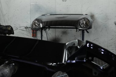Fotoğraf bir otomotiv atölyesinin sahnesini yakalıyor ve çeşitli araba parçalarını boyama sürecini gözler önüne seriyor. Araç kaputunun farklı parçaları, tamponlar, küçük detaylar..