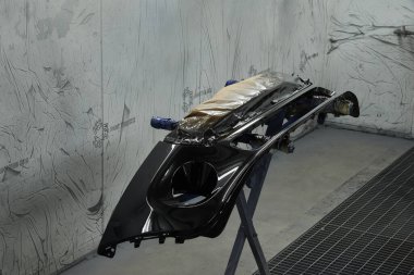 Fotoğraf bir otomotiv atölyesinin sahnesini yakalıyor ve çeşitli araba parçalarını boyama sürecini gözler önüne seriyor. Araç kaputunun farklı parçaları, tamponlar, küçük detaylar..