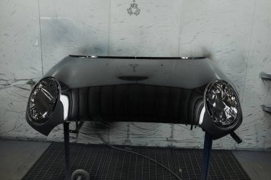 Fotoğraf bir otomotiv atölyesinin sahnesini yakalıyor ve çeşitli araba parçalarını boyama sürecini gözler önüne seriyor. Araç kaputunun farklı parçaları, tamponlar, küçük detaylar..