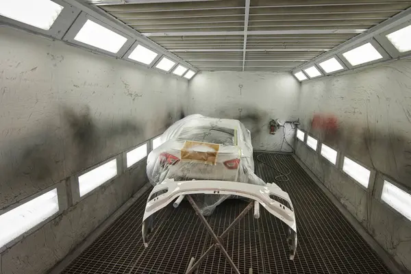Fotoğraf bir otomotiv atölyesinin sahnesini yakalıyor ve çeşitli araba parçalarını boyama sürecini gözler önüne seriyor. Araç kaputunun farklı parçaları, tamponlar, küçük detaylar..
