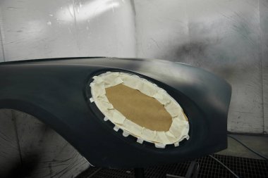 Fotoğraf bir otomotiv atölyesinin sahnesini yakalıyor ve çeşitli araba parçalarını boyama sürecini gözler önüne seriyor. Araç kaputunun farklı parçaları, tamponlar, küçük detaylar..