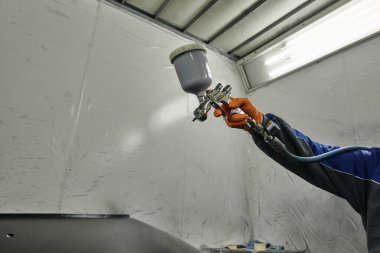 Fotoğraf bir otomotiv atölyesinin sahnesini yakalıyor ve çeşitli araba parçalarını boyama sürecini gözler önüne seriyor. Araç kaputunun farklı parçaları, tamponlar, küçük detaylar..