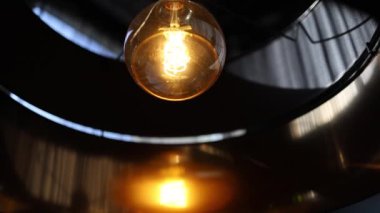 Videoda bir restoranda, yumuşak, altın bir parıltı saçan dekoratif bir lambanın yer aldığı sıcak ve ortam manzarası gösteriliyor. Büyüleyici ışık davetkar bir atmosfer yaratır..