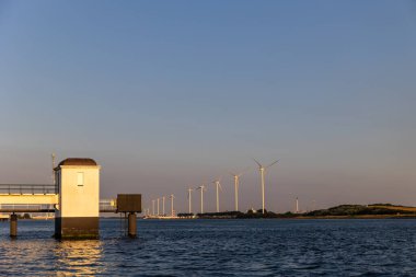 Rotterdam limanındaki güzel yel değirmenleri. Deniz kıyısında güzel bir gün batımı. Mavi Kuzey Denizi ve Su Yüzeyi. Deniz feneri ve sahil gün batımı güneşiyle aydınlanır..