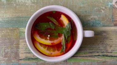 Meyve çaylı beyaz fincanın güzel üst manzarası. Kırmızı meyve çayı, birkaç dilim limon. Bir fincanda çay ve nane yaprakları var..