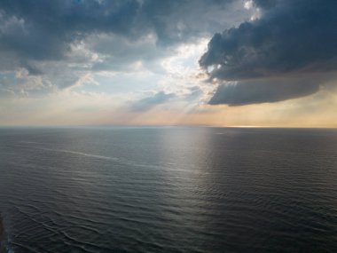 Denizin üzerinde güzel bir gün batımı, okyanus. Bir kuadkopterin üst görüntüsü. Güzel uçuş. Gemiler ve yel değirmenleri ufukta. Güneş ışınları bulutları delip geçiyor..