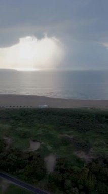 Denizin üzerinde güzel bir gün batımı, okyanus. Bir kuadkopterin üst görüntüsü. Güzel uçuş. Gemiler ve yel değirmenleri ufukta. Güneş ışınları bulutları delip geçiyor..