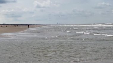 Yazın Katwijk aan Zee sahilinin güzel manzarası. İnsanlar deniz kenarında dinleniyor. Turistler için evler. Plaj şemsiyeleri, gezintiler, denizde yüzen insanlar. Hollanda 'da bir plaj. Kuzey Denizi.