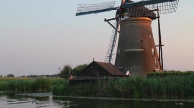 Hollanda 'nın Kinderdijk köyünde günbatımında güzel ahşap yel değirmenleri. Rüzgar değirmenleri esiyor. Güzel Hollanda kanalları suyla doludur. Güzel gün batımı.