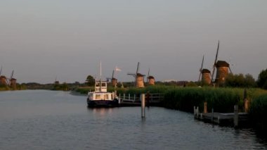 Hollanda 'nın Kinderdijk köyünde günbatımında güzel ahşap yel değirmenleri. Rüzgar değirmenleri esiyor. Güzel Hollanda kanalları suyla doludur. Güzel gün batımı. Beyaz zevk teknesi.