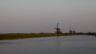 Hollanda 'nın Kinderdijk köyünde günbatımında güzel ahşap yel değirmenleri. Rüzgar değirmenleri esiyor. Güzel Hollanda kanalları suyla doludur. Güzel gün batımı.