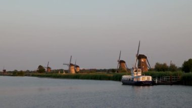 Hollanda 'nın Kinderdijk köyünde günbatımında güzel ahşap yel değirmenleri. Rüzgar değirmenleri esiyor. Güzel Hollanda kanalları suyla doludur. Güzel gün batımı. Beyaz zevk teknesi.