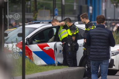 Utrecht, Utrecht bölgesi, Hollanda - 19.05.2024: Üç polis memuru işaretli bir polis aracının yanında duruyor, biri açık kapıya eğiliyor. Yüksek görünürlüklü yelek giyiyorlar..